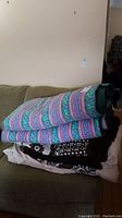 Folded stack of linens showing the colorful King size duvet on top and other linens underneath on a couch.