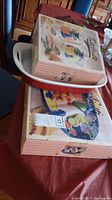 Photo showing boxed oil and vinegar set and boxed oval ceramic platter with fruit and vegetable design, and ceramic baking pan placed on a table.