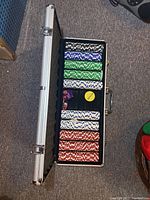 Open hard metal case displaying neatly stacked poker chips in blue, green, white, and red colors along with dice and dealer button.
