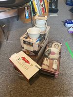 Photo showing Corelle dishes, a ceramic pot with glass lid, and boxed tea cup set on floor.