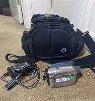 Sony DCR-HC28 camcorder with power supply charger and black carrying case arranged on floor surface.