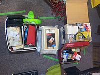 Two open boxes containing assorted stationery and office supplies, including pens, markers, reels of tape, and picture frames visible in both boxes.