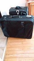 Photo showing two black fabric suitcases on wooden floor, one showing front zipper pull missing.