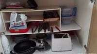 Kitchen items including frying pans, pots, utensils, and Black and Decker toaster under a counter.