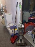 Overall view of the vacuum and carpet sweeper in basement environment alongside other household items.