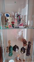 Two shelves inside a display case containing various collectible items including glass etchings, Portuguese rooster ceramics, and assorted wood and rock carvings.