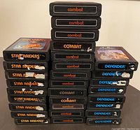 Stacked cartridges showing labels Combat, Defender, Star Raiders with label wear and sticker damage on some cartridges.