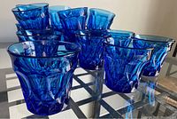 12 vintage Noritake blue tumbler glasses arranged on a glass table, showing the textured faceted design and deep blue color.