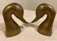 Pair of brass duck head bookends positioned facing each other on a light surface.