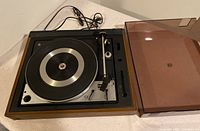 Overview of Dual 1225 turntable with its dust cover placed beside it on the right, showing wood grain side panels and controls.