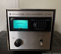 Front view of Kenwood Audio De-Noiser KF-6011 showing the VU meter lit in green, the power knob, noise level slider, and tape monitoring toggle switch.