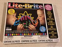 Front image of the Lite-Brite Ultimate Edition box showing the brand name, age recommendation (4+), number of pieces (262), features such as colorful light pegs, templates, and magic screen.