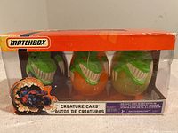 Front view of boxed set showing three green dinosaur egg-shaped containers with cars inside, packaging with Matchbox logo and product branding.