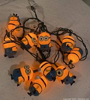 Photo of the Minions string lights illuminated, showing multiple Minions characters connected by green wiring and plugged in.