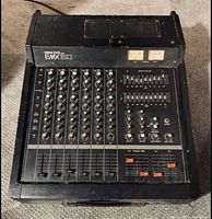 Full view of Yamaha EMX150 mixer showing multiple input channels, sliders, knobs, and VU meters with visible wear and dust.