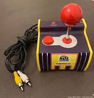 Namco TV Game joystick controller with red spherical joystick, red button, reset button, on/off switch, and RCA audio/video cables connected and coiled beside it, photographed from the side.