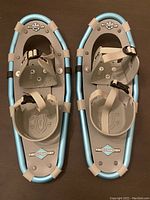 Front view of the pair of children's snowshoes in light blue and beige with adjustable straps