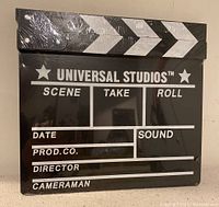 Front view of the Universal Studios clapper board, sealed in plastic, showing writing sections and clapper arm with black and white design.