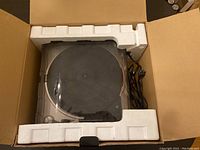 Top view of the USB turntable inside open box with styrofoam packing and power cord visible