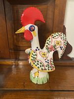 Front-angle photo of a hand-painted Portuguese ceramic rooster with a red comb, yellow beak, and colorful floral decorations on the body placed on a wooden surface.