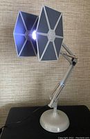 Angled side view of Star Wars TIE Fighter task light with articulated arm, showing lit cockpit as light source.