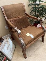 Full front angle showing armchair upholstery, carved wooden arms with silver accents, and decorative pillow.
