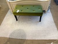 Green velvet tufted bench with dark legs placed on a white rug in a bedroom setting.