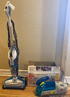 Bissell CrossWave floor cleaner upright with Dirt Devil Spot Scrubber and Dirt Devil box next to it on wood floor.