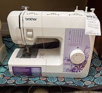 Front view of white Brother LX2763 sewing machine with purple floral decal and cloth cover underneath.