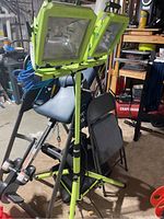 Photo showing the full adjustable double work light on tripod stand in basement setting with other tools and equipment in background.