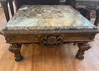 Front view of square coffee table showing faux stone top and carved wooden base.