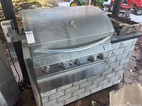 Front view of stainless steel grill with four control knobs and faux stone cart