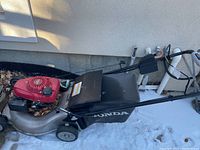 Side view of Honda self-propelled gas lawn mower showing black grass catcher and red motor cover with Honda branding.