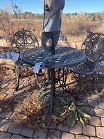 Front view of round iron patio table, two matching chairs, umbrella covered and base visible beneath table on patio stones.