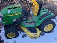 Side profile showing green body, yellow wheels, and 48" deck with leaf and snow debris