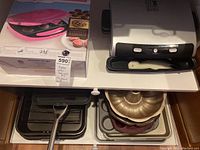 Lot contents on table showing George Foreman grill, Baby Cakes cupcake maker box and multiple baking items