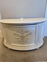 Front view of white decorative storage chest showing overall shape and floral relief.