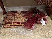 Pile of assorted table linens including tablecloths and placemats with varied patterns and fringe trim.