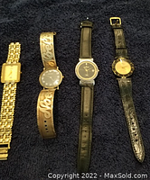 Four vintage watches laid on dark fabric: one gold-tone link band, one wide silver-gray decorative band, and two with black bands, all show signs of wear.