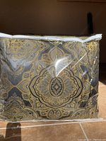 Comforter featuring an elaborate gold and gray pattern with intricate floral and circular designs, packaged in clear plastic.