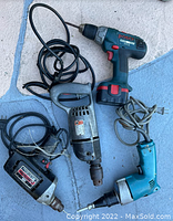 Top view of five electric drills with cords on stone surface, showing different brands and types including Bosch and Craftsman.
