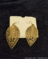 Pair of gold-tone double leaf hanging earrings on a white card against black fabric, showing detailed leaf design with small crystal accents.