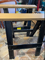 Close-up image of one folding saw horse showing black steel legs and wooden plank top with adjustable height mechanism.