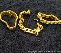 Three gold plated men's bracelets displayed on black fabric background, showing varied chain styles and sizes.