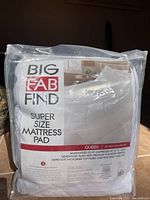 Photo of a Big Fab Find queen size mattress pad in its original clear plastic packaging showing the brand and product details.
