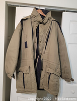 Beige men's winter coat hanging on wooden hanger showing front with pockets and high collar.