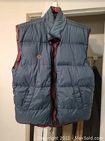 Blue sleeveless puffer jacket with burgundy interior lining, front zipper, stand-up collar, and two front pockets