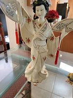 Front angle of vintage porcelain Geisha figurine showing kimono details and a fan with red tassel.