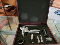 Top-down view of the open wooden box containing wine bottle opening tools arranged in foam insert.