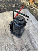 Side view of black 20 ton bottle jack with red handle resting on wooden platform.